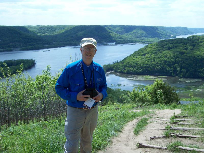 Don Leaon holding a camera in front of a river landscape