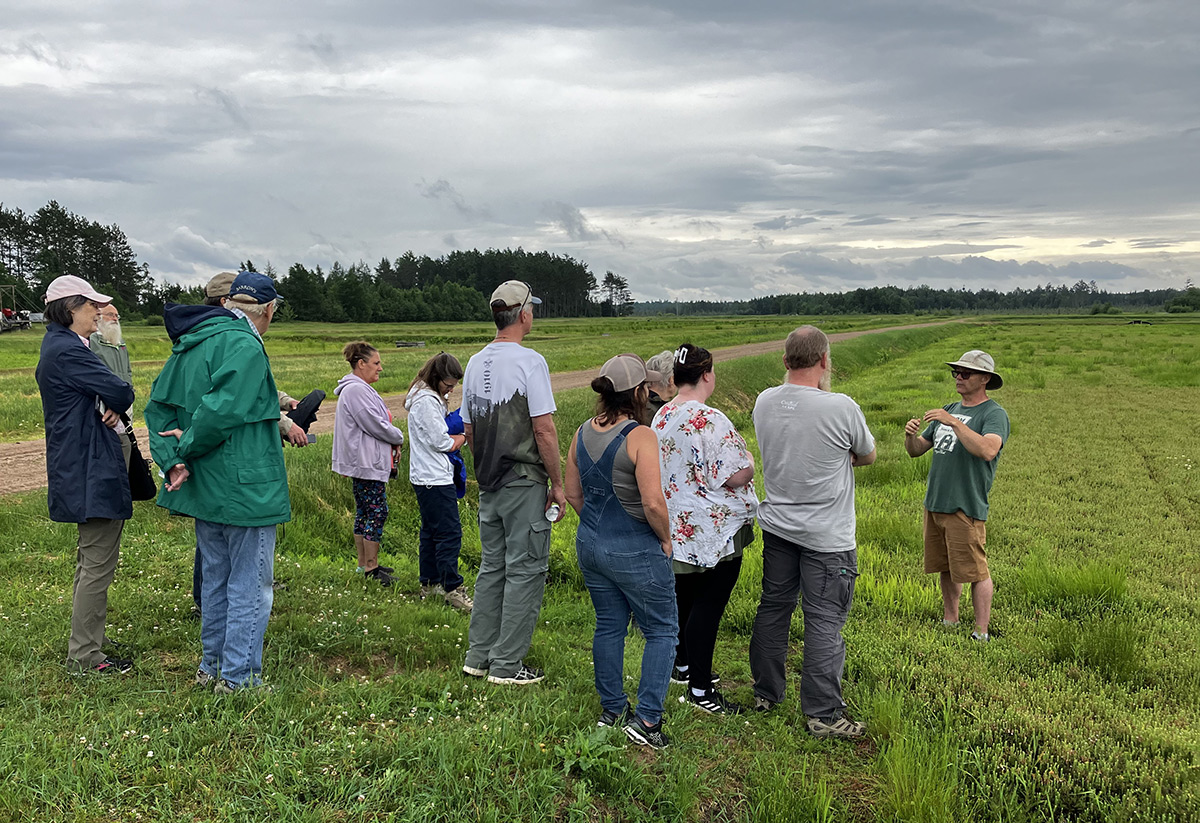 A group of people stand in a field listening to a man