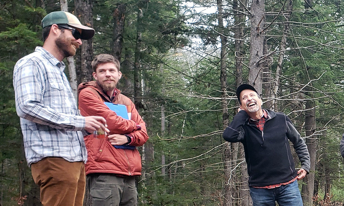 3 people smile and converse in the forest