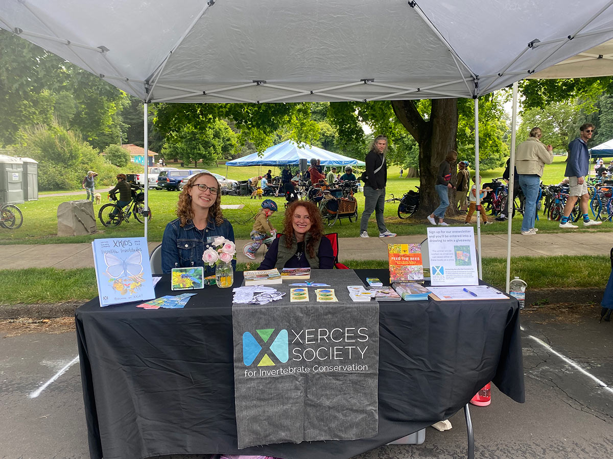 Two women, Sierra Enright and Lisa Loving, sitting behind a Xerces table display at a community event.