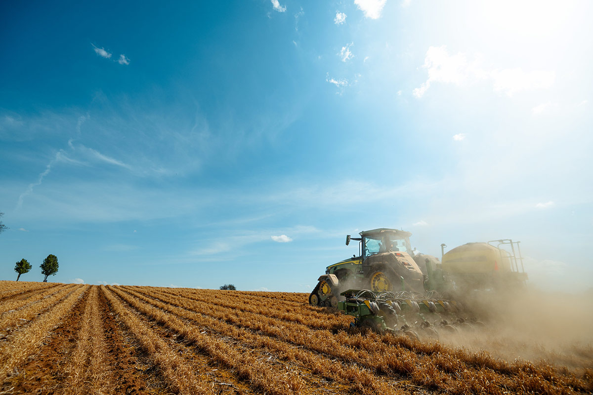 A tractor with a seed-planting attachment drives through a field, planting corn seeds behind it as it travels.