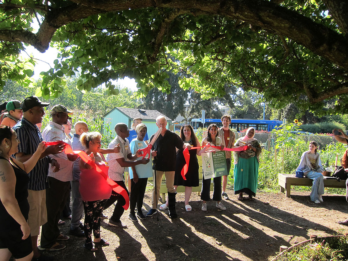 Community members cutting a giant ribbon with giant scissors at the garden