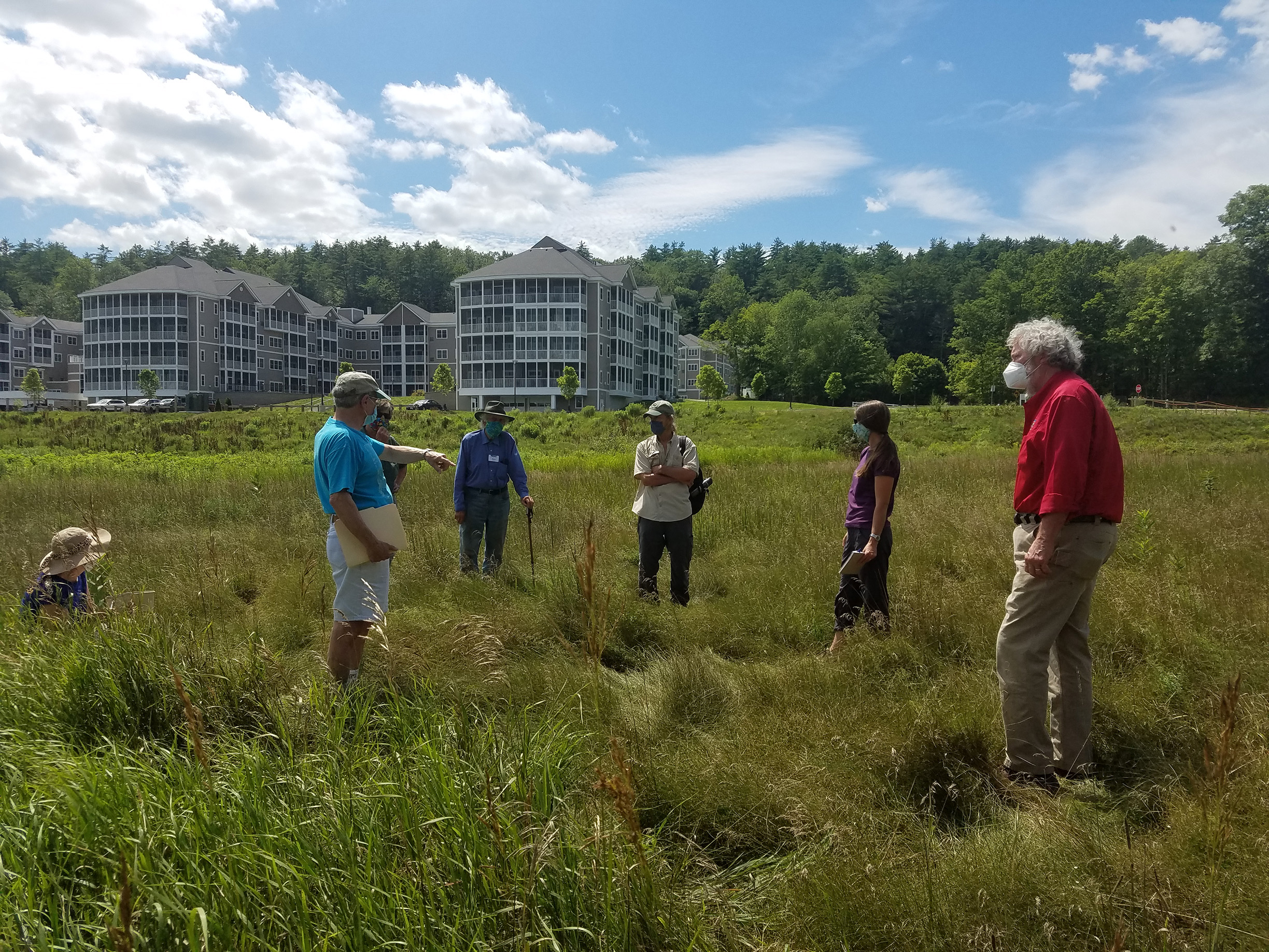 A group of men and women stand in the middle of an old hayfield discussing plans for restoring wildflowers.