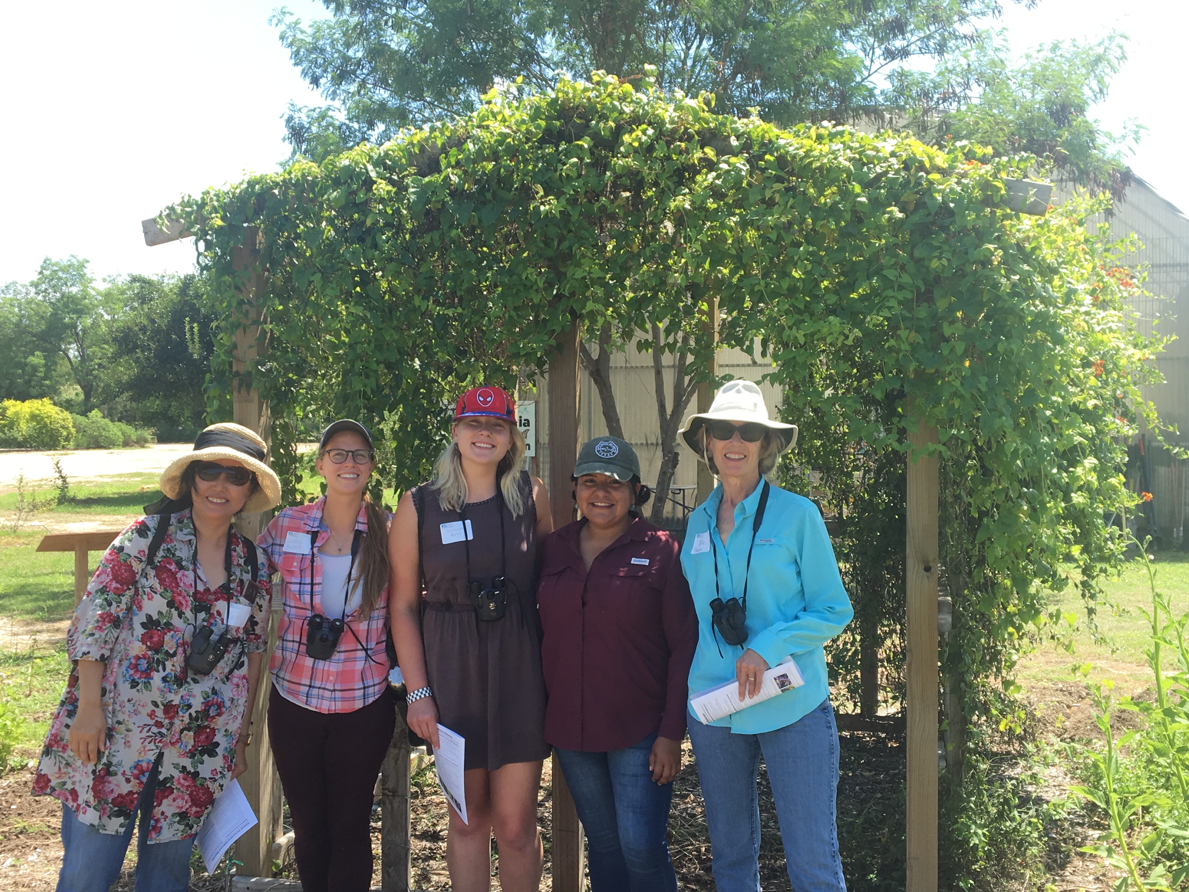 A group of smiling people pose in a garden setting.