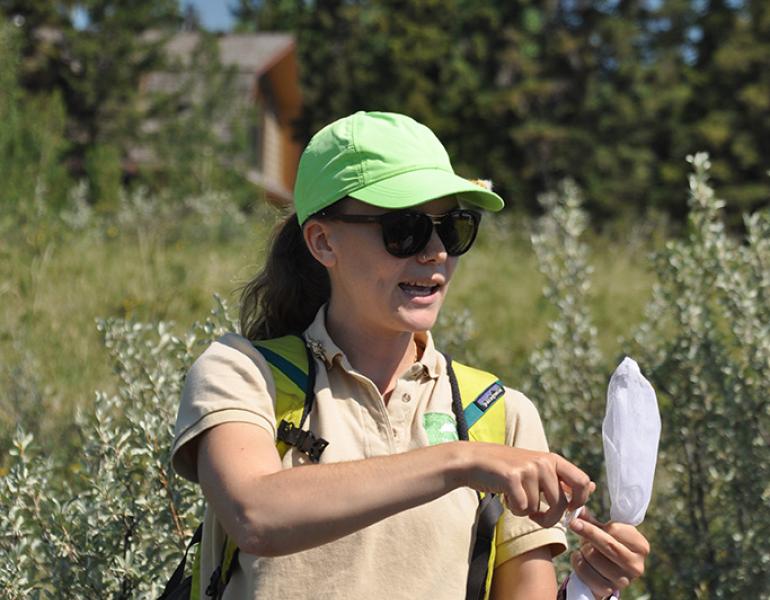 The author stands in a field holding a net while talking during a demonstration.