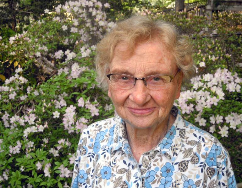 A smiling woman in front of a blooming bush