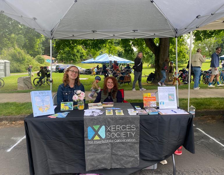 Two women, Sierra Enright and Lisa Loving, sitting behind a Xerces table display at a community event.