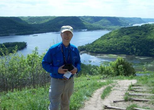 Don Leaon holding a camera in front of a river landscape