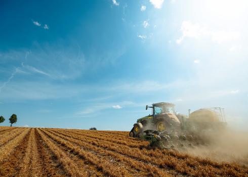 A tractor with a seed-planting attachment drives through a field planting corn seeds behind it as it travels.
