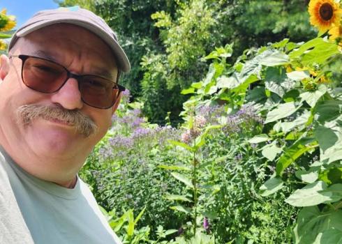 Michael McIntyre smiling in front of tall flowering plants like sunflowers