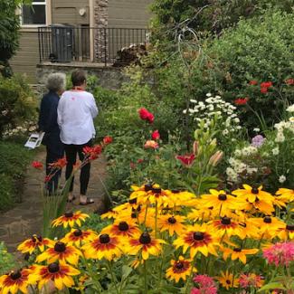 Two women walk through a garden with abundant, colorful flowers.