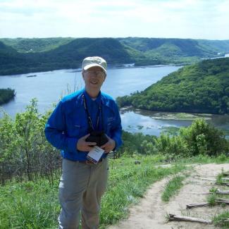 Don Leaon holding a camera in front of a river landscape