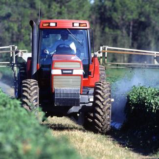 Tractor applying pesticides to rows of crops