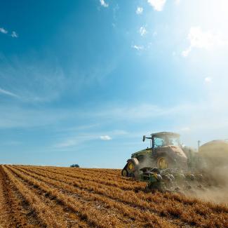 A tractor with a seed-planting attachment drives through a field planting corn seeds behind it as it travels.