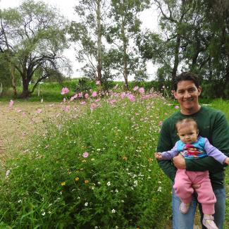 The author, Héctor Ávila Villegas, stands beside a pollinator habitat strip full of pink, white, and yellow flowers