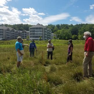 A group of men and women stand in the middle of an old hayfield discussing plans for restoring wildflowers.