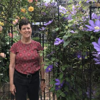 Jan Mooney stands beside purple clematis and yellow rose vines at Upper Fells Point Community Garden