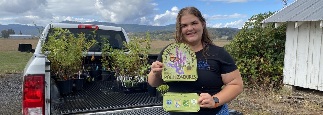 Habitat Kit participant with plants and pollinator habitat sign at OR distribution day. 